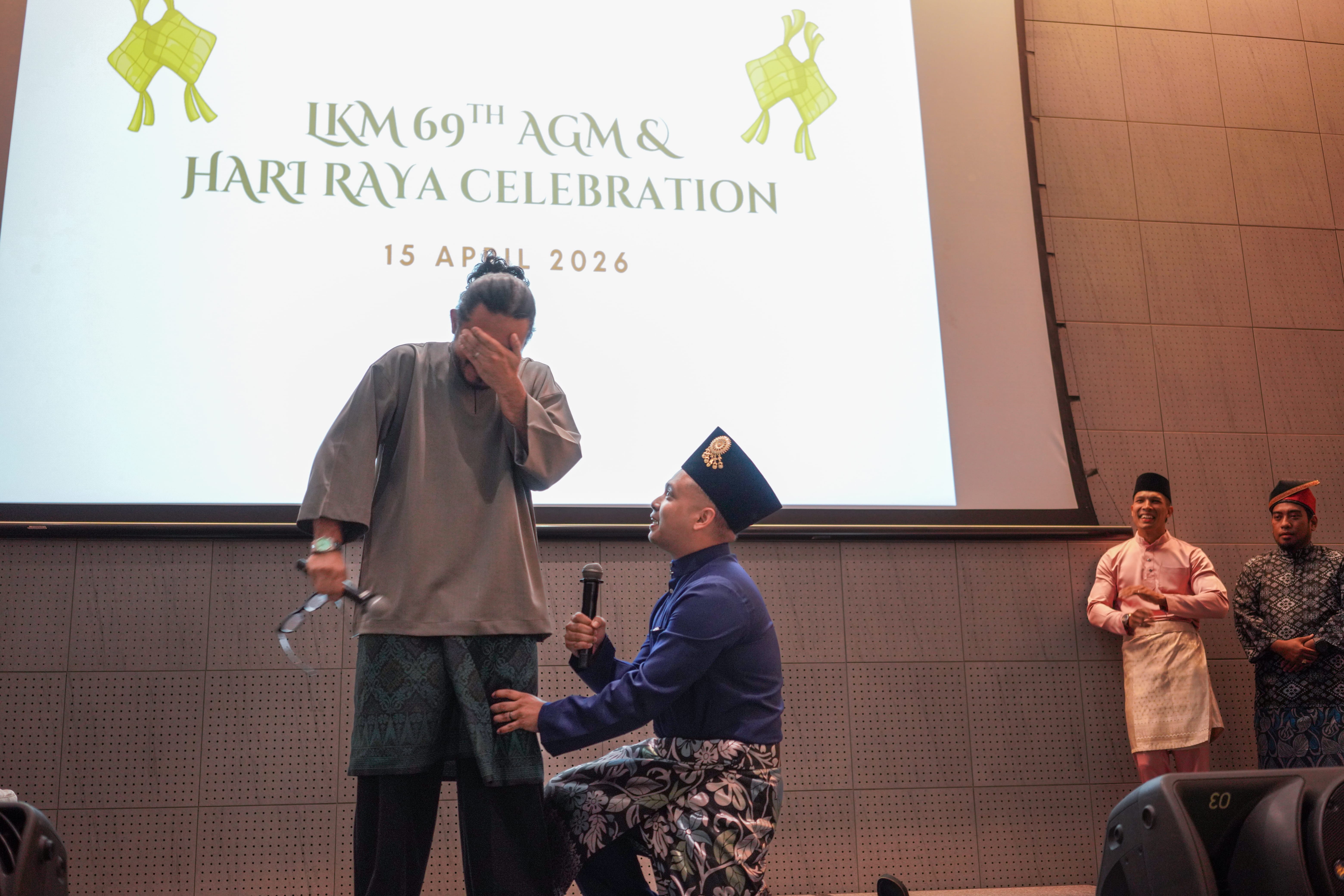 Two performers acting out a comedic scene on stage while other participants watch from the background.